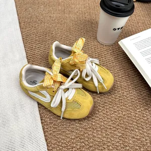 Detailed view of yellow girls' mesh sneakers featuring stylish ribbon bows and soft soles.