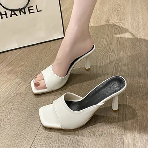 Detailed side view of elegant white square toe high heel mules on rustic wooden floor
