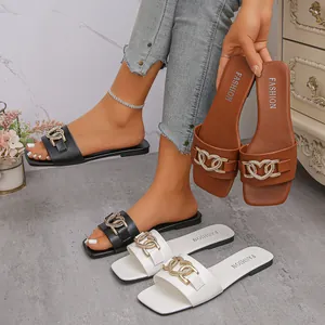 Eleganti sandali piatti da donna con catena dorata a cuore in nero, marrone e bianco.