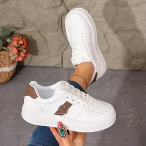 Detalle de zapatillas blancas con plataforma para mujer con hebilla de corazón decorativa.
