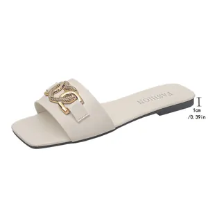 Dettaglio di sandali bassi beige con fibbia a catena dorata e tacco da 1 cm.