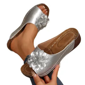 Sandales compensées argentées pour femmes avec grande fleur métallique décorative.