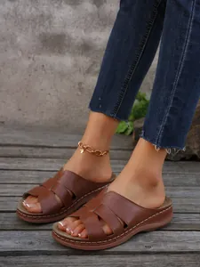 Detalle de sandalias de cuña marrones usadas en una plataforma de madera con jeans