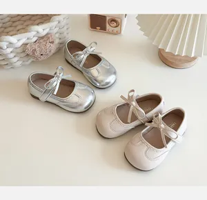 Silver and beige children's Mary Jane shoes with decorative bows on a white surface