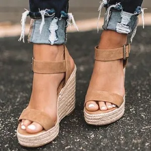 Close-up worn view of stylish tan suede wedge sandals with ankle strap and espadrille heel