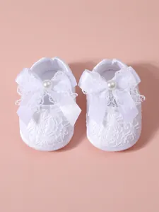 Detail view of white lace newborn girl shoes featuring a soft bow and pearl accent.
