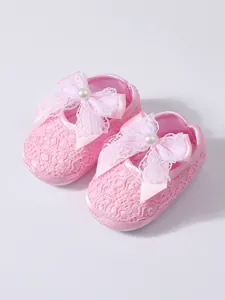 Close-up detail view of pink lace baby shoes with soft soles and white bow decor