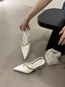 Close-up detail of white pointed-toe slingback heels with a gold metallic strap decoration