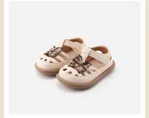 Detailaufnahme cremefarbener Kleinkind-Sandalen mit karierter Schleife und Lochmuster