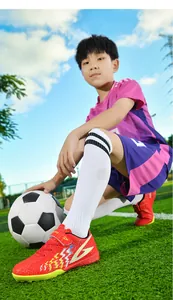 Bambino che indossa scarpe da calcio rosse antiscivolo con velcro su erba artificiale.