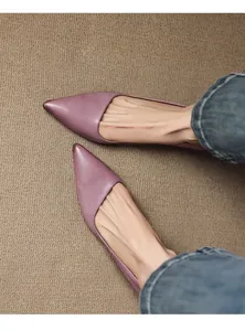 Close-up of elegant purple pointed-toe pumps worn with blue jeans on a textured rug