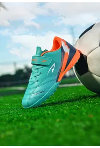 Chaussure de football TF turquoise pour enfant sur terrain d'herbe verte avec ballon