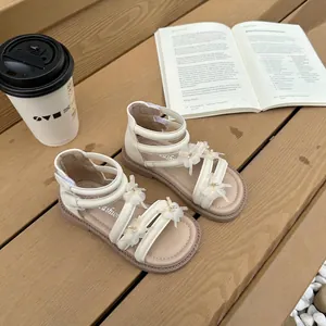 Detailansicht cremefarbener Mädchensandalen mit Schleifen und Perlen auf Holz