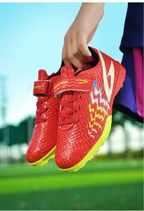 Primo piano di scarpe da calcio rosse per bambini con tacchetti gialli su un campo