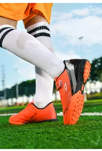 Chaussures de football orange pour enfants avec crampons TF pour terrains synthétiques.