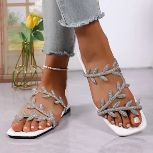 Detailed view of white flat sandals featuring rhinestone leaf straps and square toe.