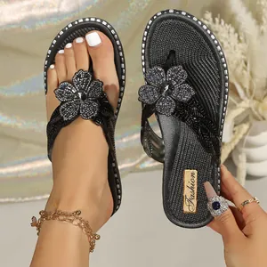 Close-up detail of black summer flip-flops featuring beaded flower and crystal centerpiece