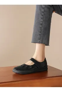 Vista detallada de zapatos planos de cuero negro con detalles florales y velcro en el pie