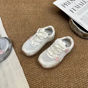 Detail of cream girls' mesh sneakers with pink flower accents on a textured rug.
