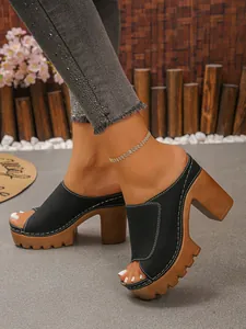 Close-up of black platform peep toe mules with chunky wood-grain heels on foot