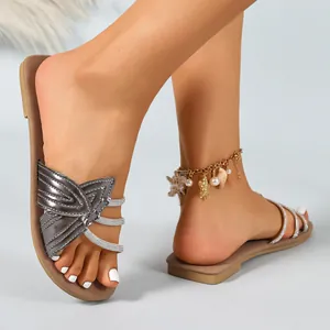 Detail view of metallic silver flat sandals with rhinestone straps and bow accent