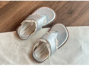 Vue détaillée de tongs argentées pour enfants avec bordure en dentelle blanche.