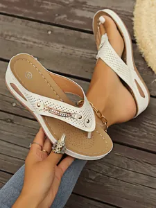 Vista detallada de chanclas blancas con cuña, decoración de cadena y tiras caladas