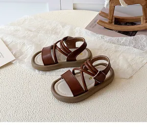 Close-up of brown children's Roman sandals with cross straps and soft anti-slip soles.