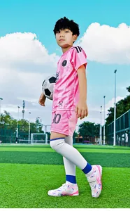 Professional action shot of young boy wearing pink and white TF soccer shoes on a green field