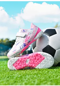Detailed macro view of pink and white kids' TF soccer shoes on a sunny soccer field