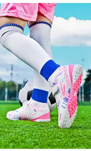 Side view of children's pink and white turf soccer shoes on a green football field.
