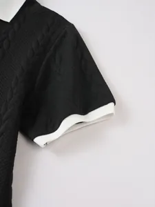 Macro detail view of black cable-knit texture and white contrast sleeve cuff on a men's polo shirt