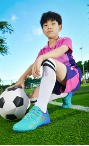 Boy wearing turquoise TF football shoes with velcro closure on a green turf field