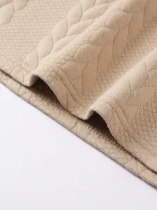 Close-up of beige jacquard knit fabric showing intricate texture and hem stitching