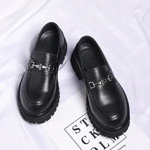 Detail shot of black chunky leather loafers with metal horsebit on white fabric background.