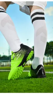 Close-up of green children's soccer shoes with Velcro and turf studs on grass.