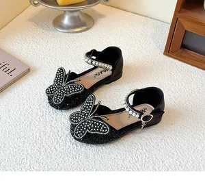 Detailed view of girls' black princess shoes featuring a large rhinestone butterfly and pearl strap