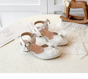 Detailed view of white children's sandals with rhinestone bow and low block heel.