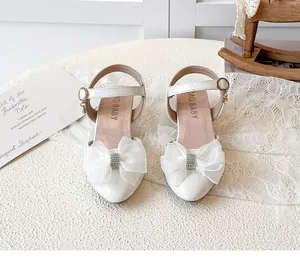 Detailed view of white children's high heel sandals with rhinestone bow