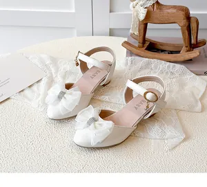 Elegant white children's high-heel sandals featuring a rhinestone bow and mesh accents
