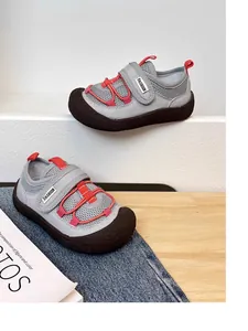 Detail view of grey children's breathable sneakers with red accents and soft brown soles.