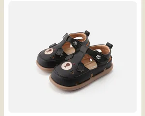 Detailopname van zwarte lederen peutersandalen met berengezicht en pootafdruk ontwerp