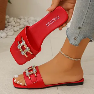 Detail of stylish red flat slide sandals with luxury rhinestone buckle and square toe design