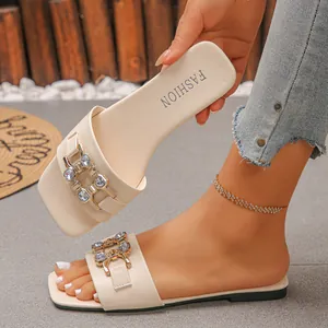 Close-up of off-white flat sandals with a rhinestone-studded gold buckle detail on strap.