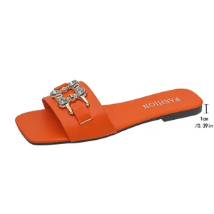 Close-up of orange flat sandal with square toe and crystal-embellished gold buckle detail.