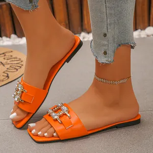 Detail of orange flat slide sandals featuring a sparkling rhinestone buckle on a model