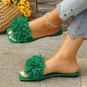 Close-up of green flat slide sandals with large ruffled fabric flower decorations.