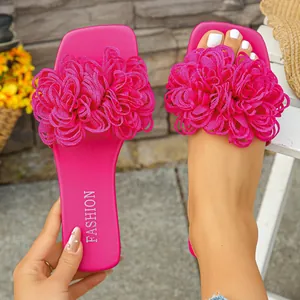 Detail view of vibrant magenta flat slippers with large 3D fabric flower decorations.