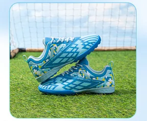 Blue children's turf soccer shoes featuring geometric patterns on a grass field.