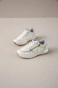 Vista detallada de zapatillas de moda blancas y plateadas con cremallera lateral y suela de goma